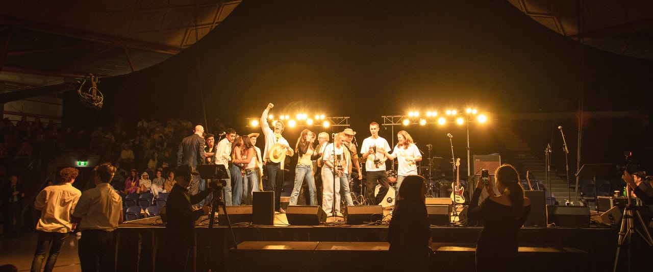 A band performs on a lit stage in front of a crowd.