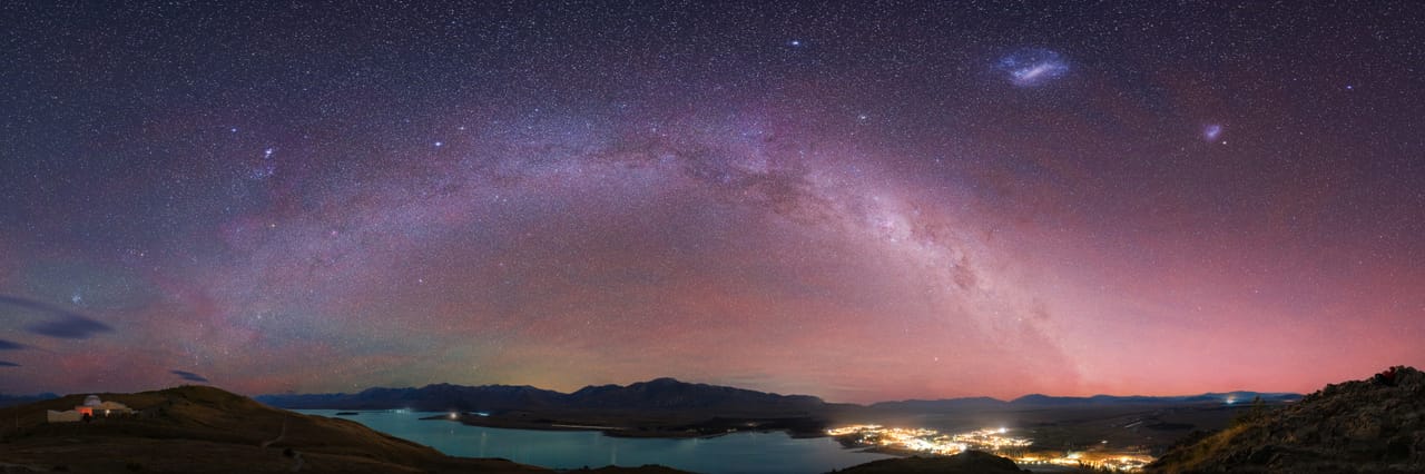 The Milky Way arches over a lake and a small town at night.