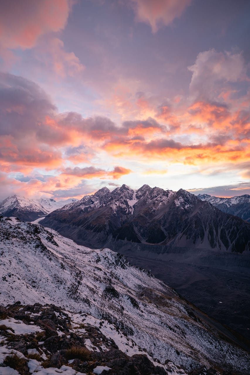 Snow-covered peaks under a pink and orange sunset sky.