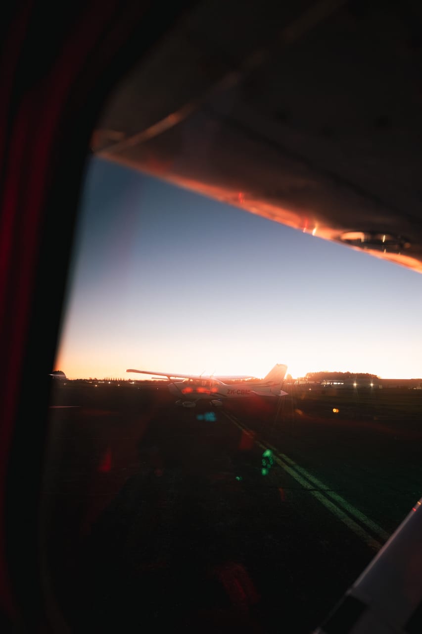 The sun sets beyond an airfield, seen from inside a small aircraft.