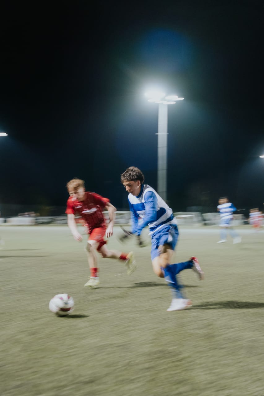 A player in blue-and-white stripes sprints past a defender in red at night.