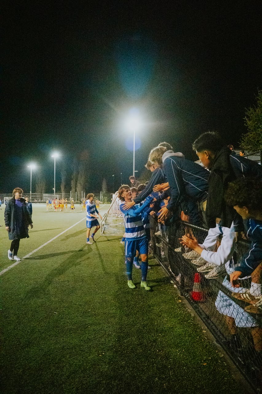 Players in blue-and-white stripes high-five supporters along the fence after a night match.