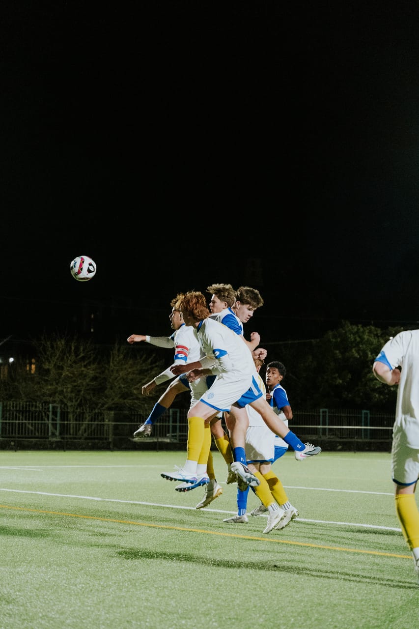 Players leap for a header under the floodlights.