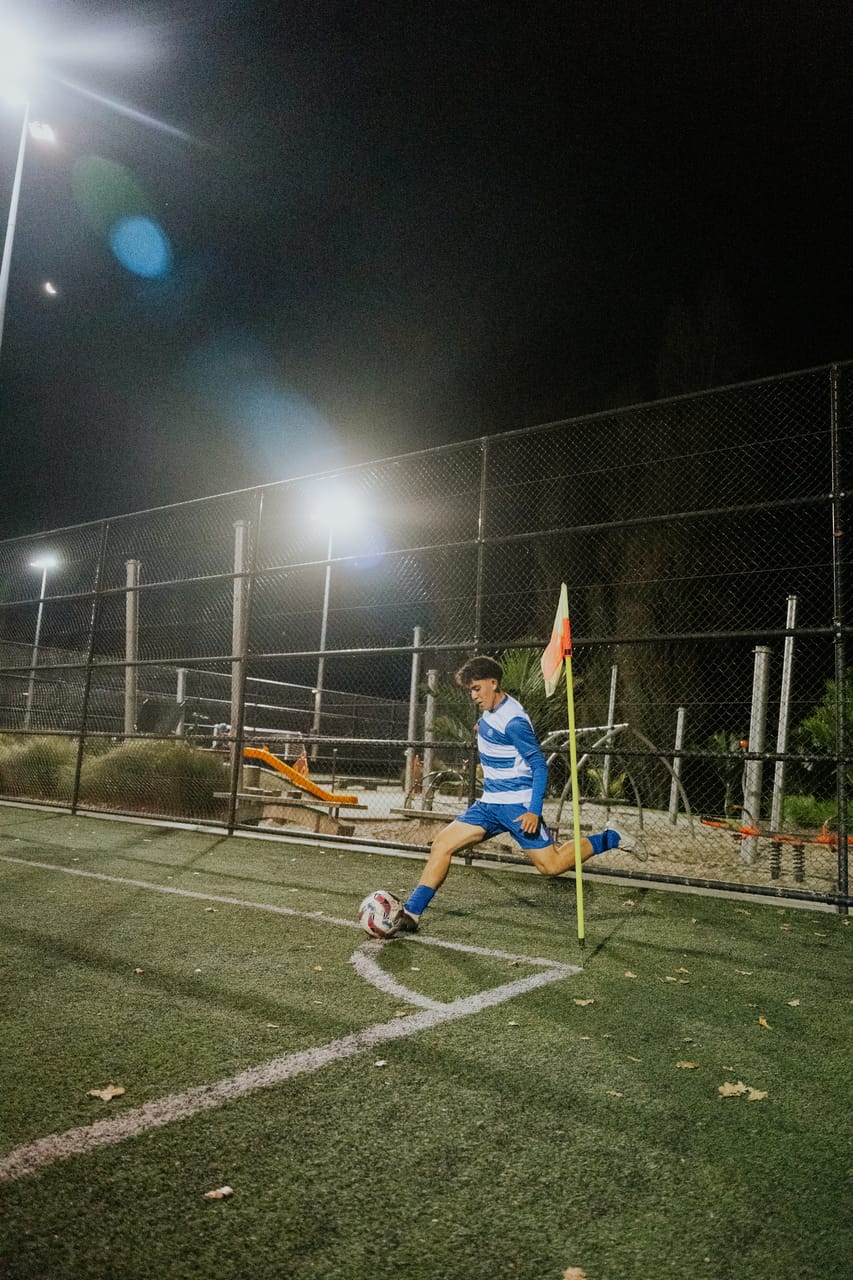 A player takes a corner kick beside the flag under floodlights.