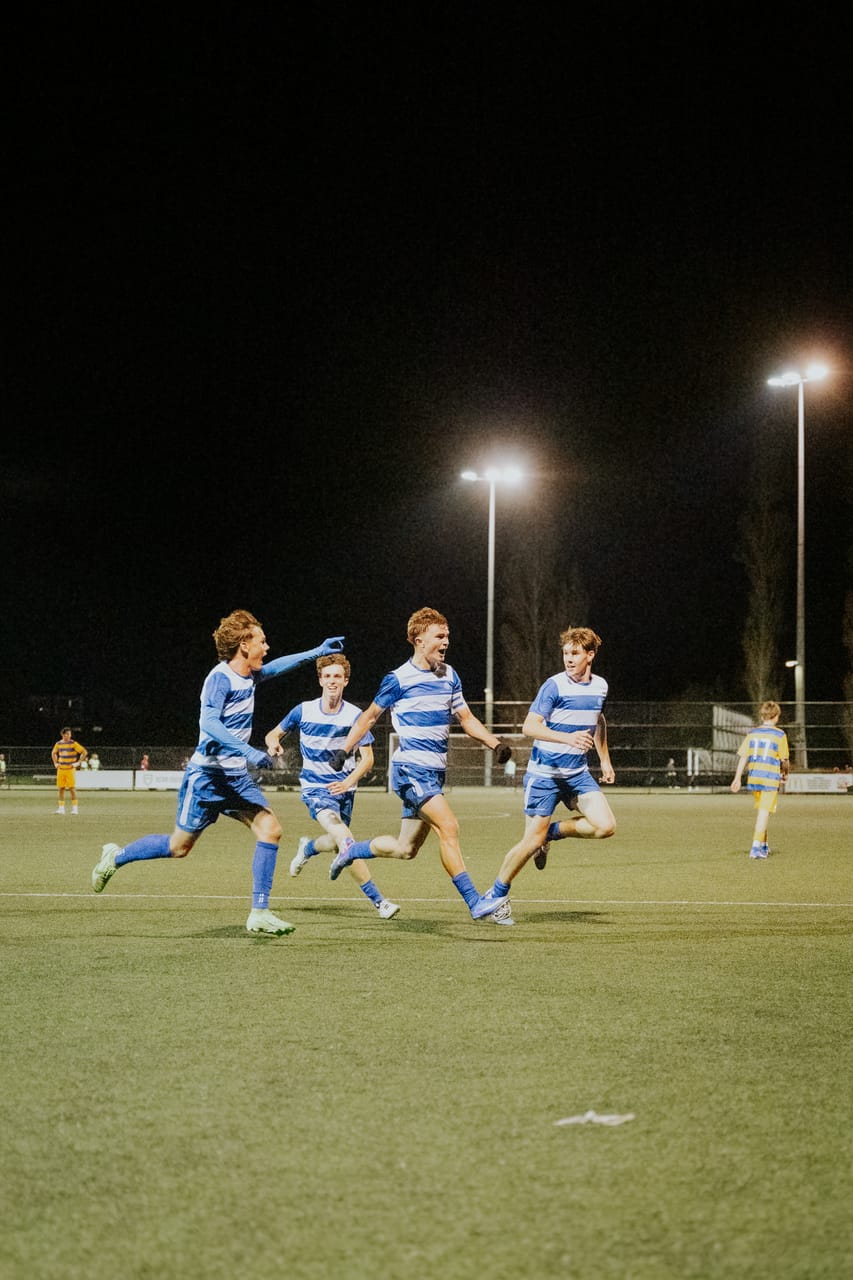 Players in blue-and-white stripes run to celebrate a goal at night.