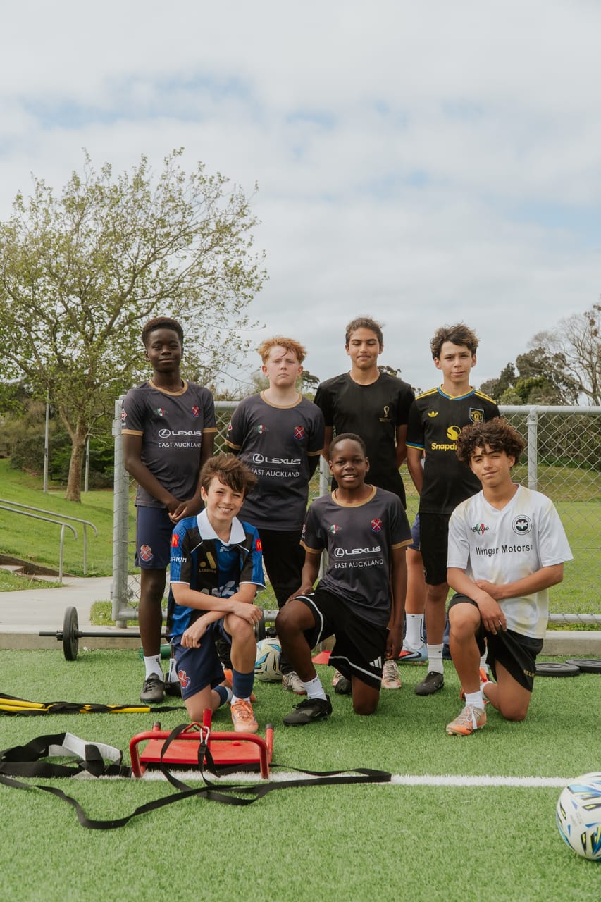 A training group poses on the pitch with their gear after a daytime session.
