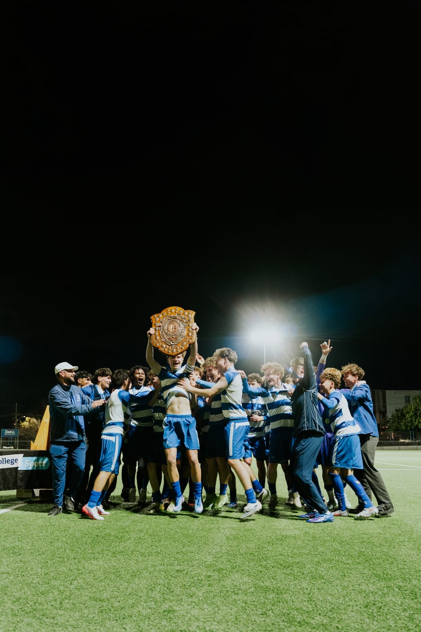 A team in blue-and-white stripes lifts a trophy shield under the floodlights.