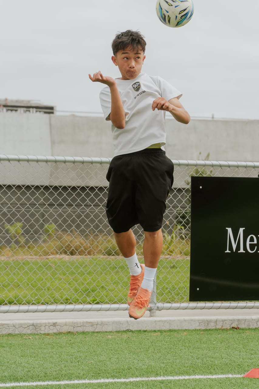 A player in white leaps to chest the ball at a daytime training session.