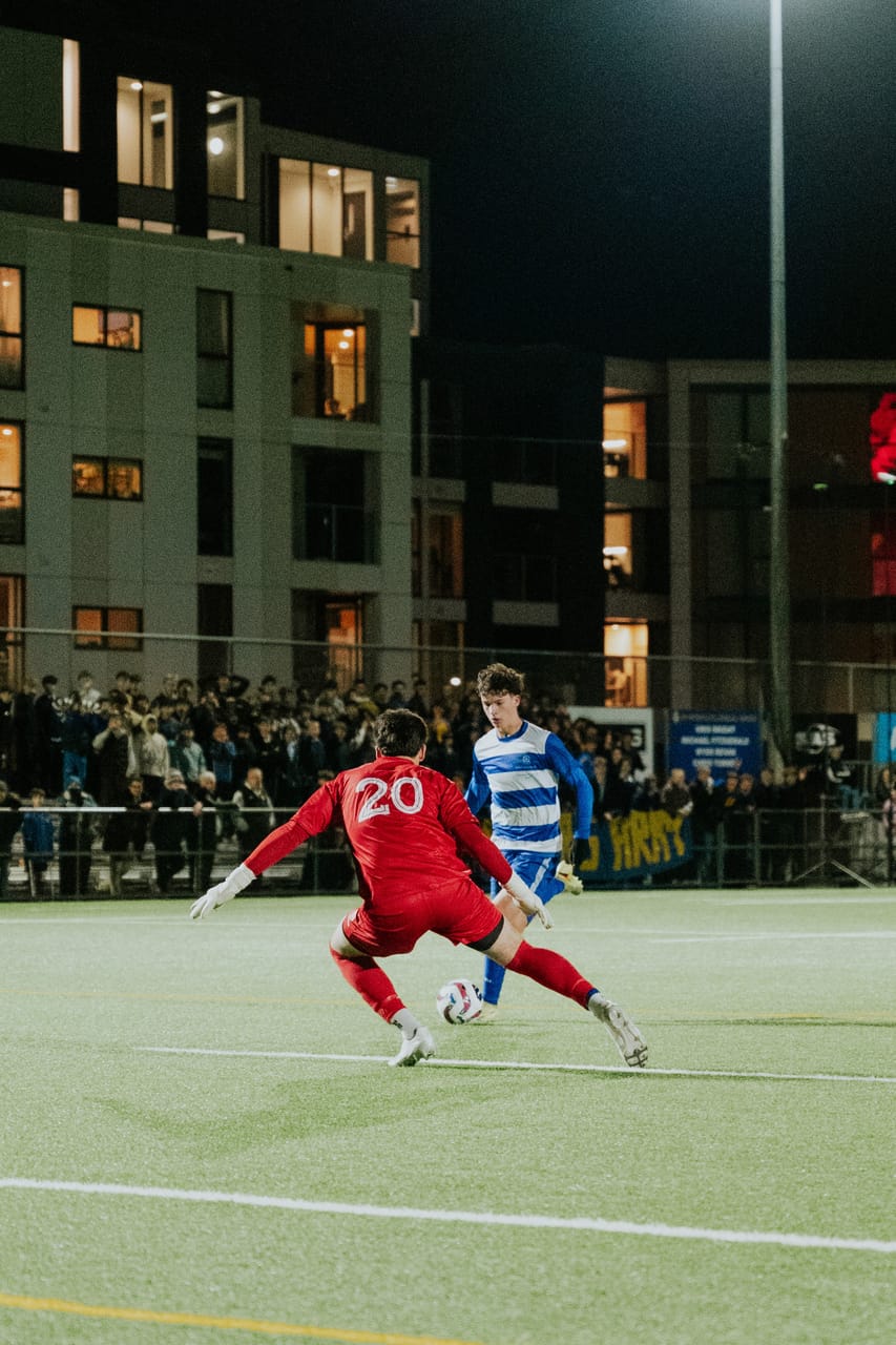 A player in red chases an attacker in blue-and-white stripes in front of a crowded stand.