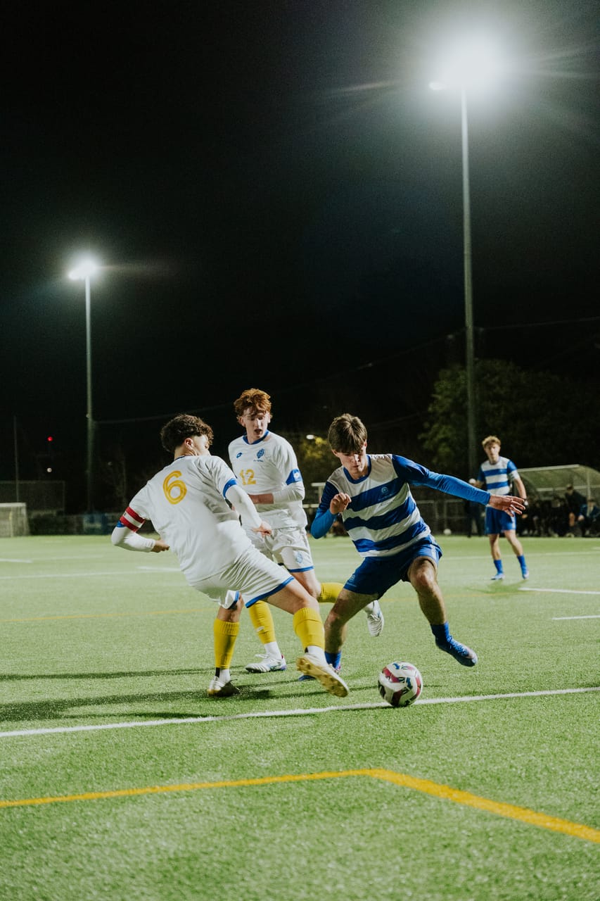 A player in blue-and-white stripes tackles an opponent in white under floodlights.